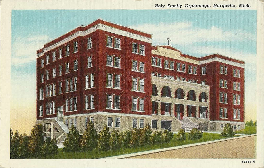 A printed postcard showing a large institutional building of several storeys with rows of identical windows, standing behind a lawn
