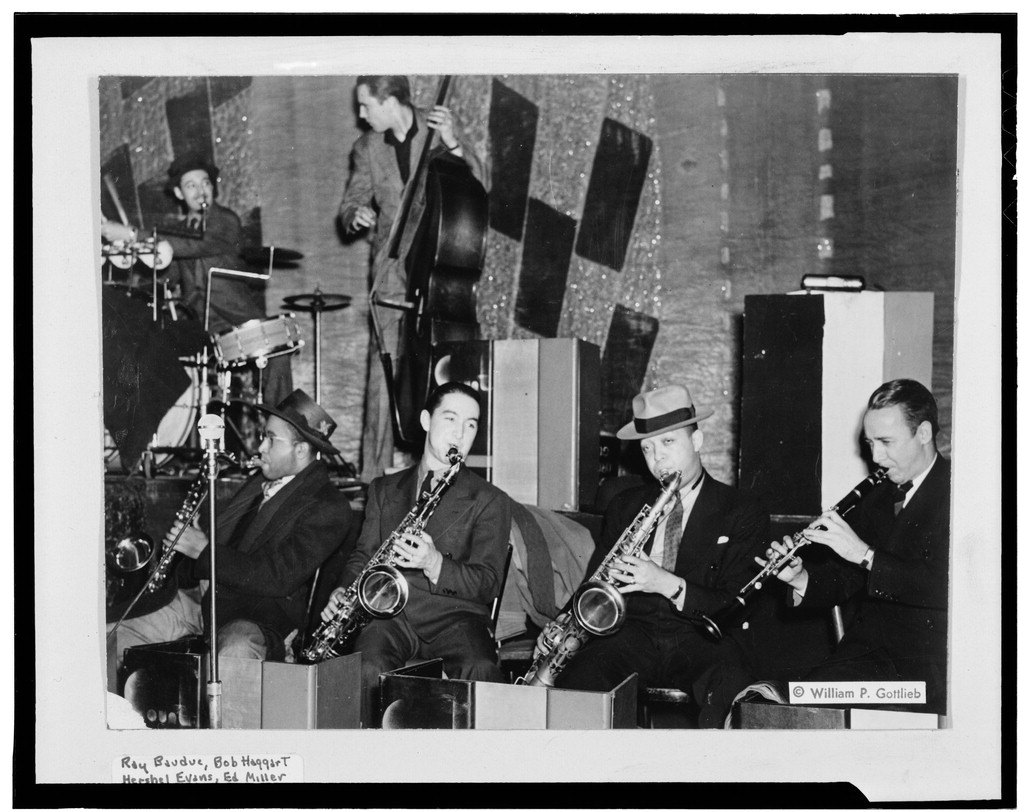 A band on a decorated stage: two saxophone players and a clarinettist seated in a row, a double bass and drums behind them