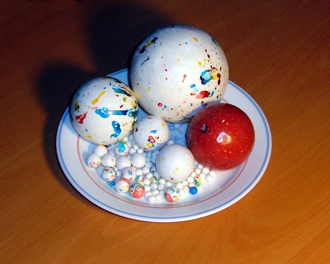 A small plate holding several large speckled jawbreakers, one deep red and the others white flecked with color, beside a scatter of tiny candy balls