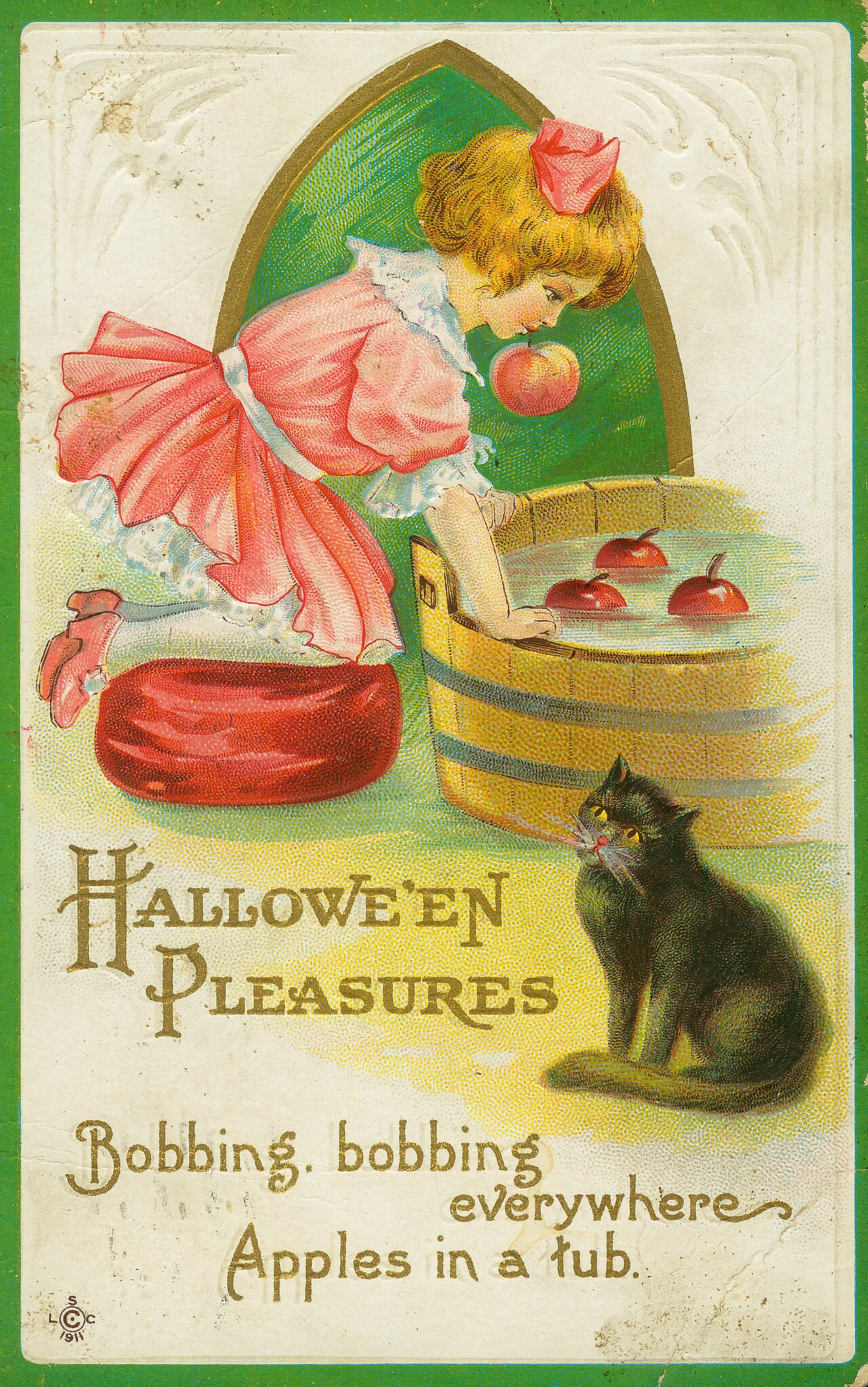 An old color postcard of a girl in a pink dress leaning over a wooden tub of water with three red apples floating in it, one apple at her lips, a black cat watching from the corner