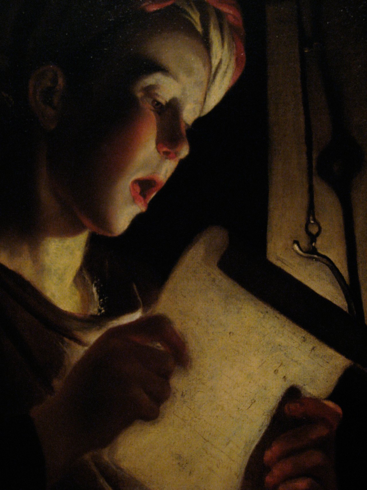 A painting of a boy singing from a sheet of music, his face and hands lit warmly by an unseen candle while everything behind him falls into darkness