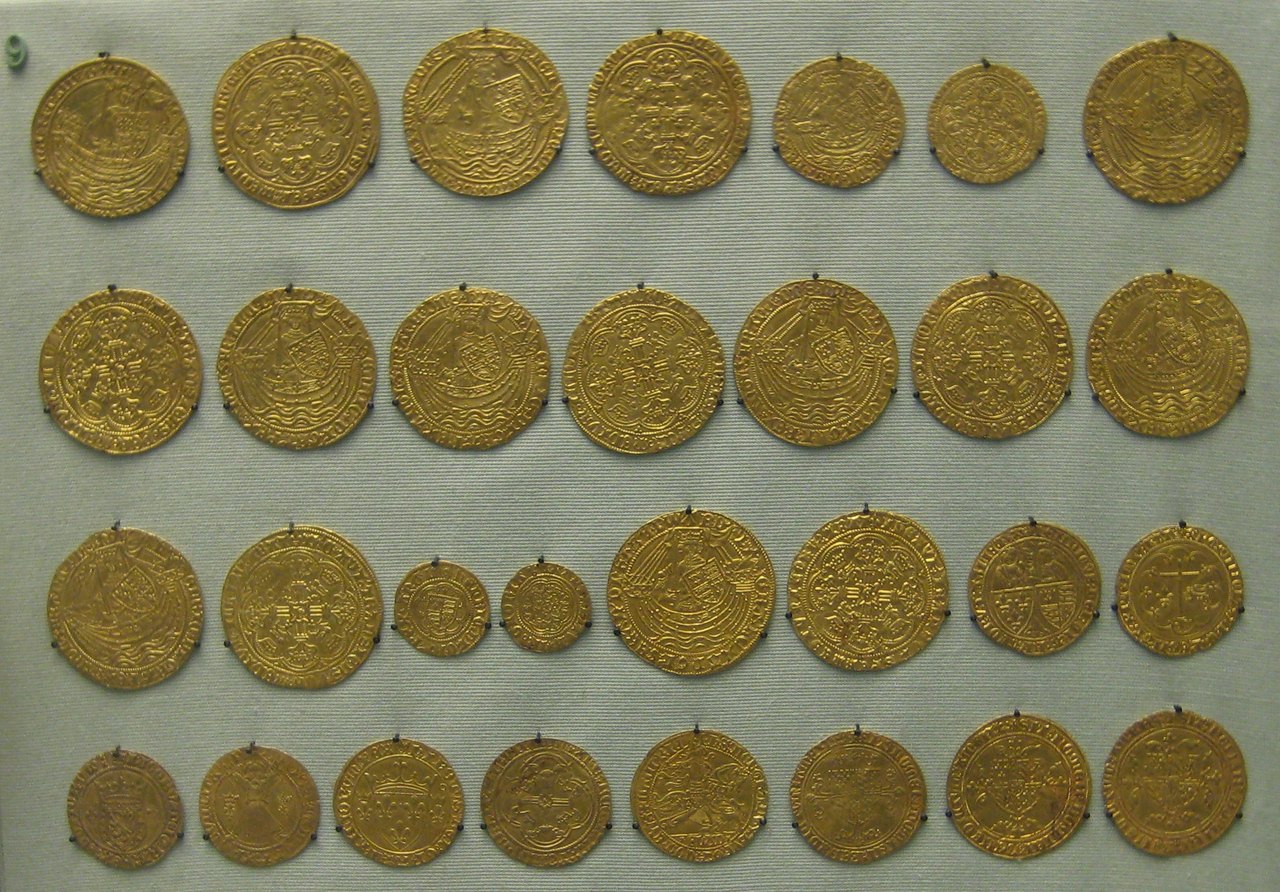 Rows of small round gold coins from a medieval hoard, laid out flat on a dark surface with their worn faces turned upward