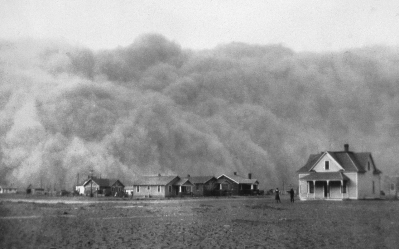 A wall of dust hundreds of feet high rolling toward a small town of low wooden houses, two figures standing in the bare yard in front of it