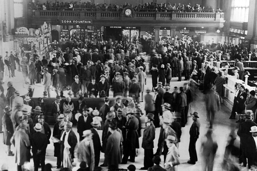 A vast railway station hall packed shoulder to shoulder with hundreds of people in coats and hats, a balcony crowded with more of them above