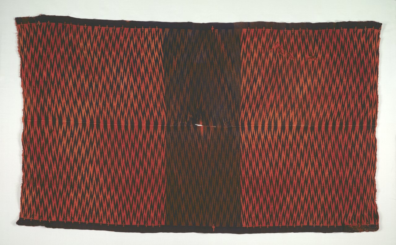 A large woven Mexican blanket covered edge to edge in fine red and black zigzag bands, with a darker panel down the middle