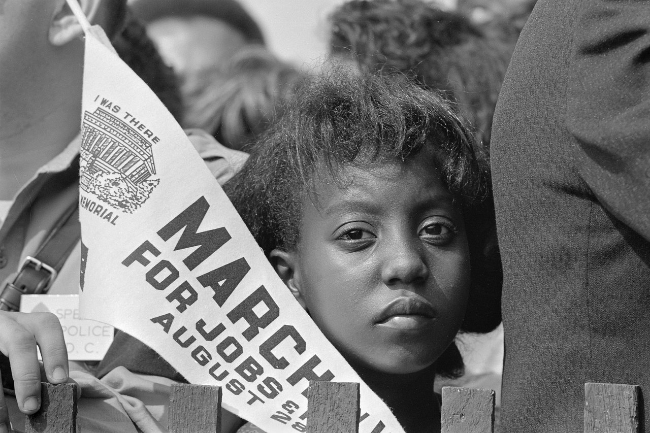 A young woman in a crowd looking steadily at the camera, holding a pennant reading March for Jobs above the words I was there