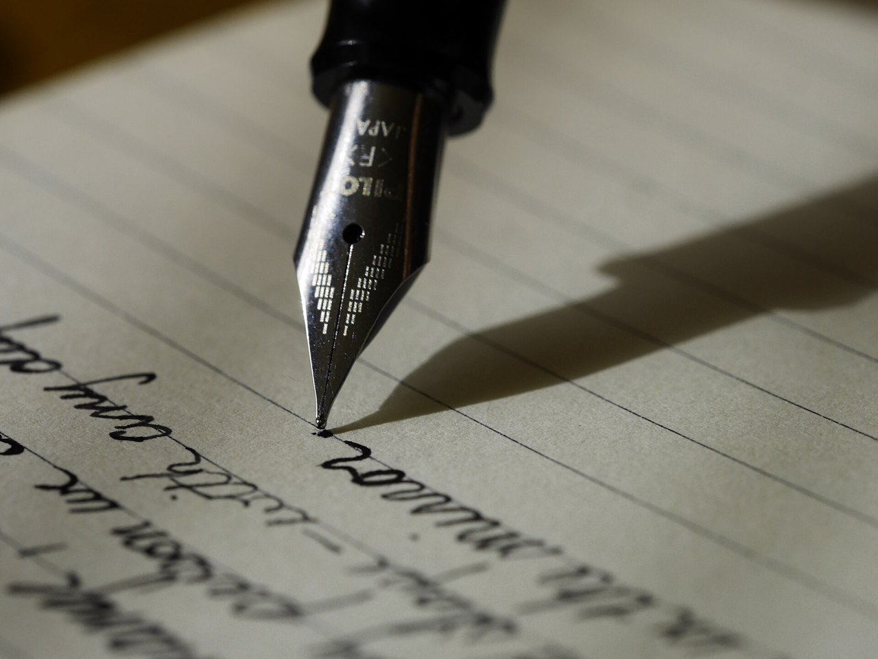 A close-up of a fountain pen's steel nib touching lined paper, with a line of handwriting in dark ink beneath it