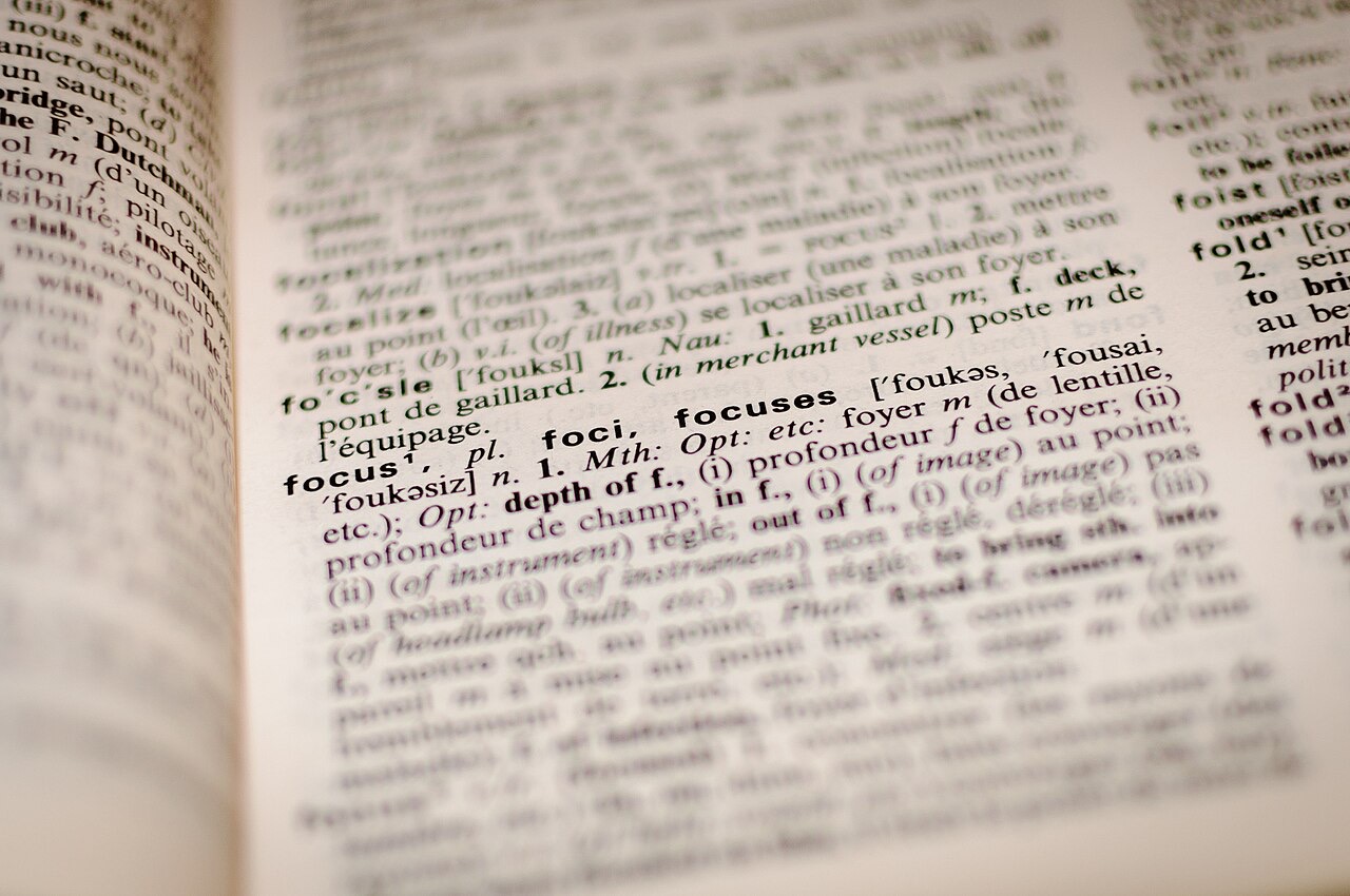 A dictionary lying open, the camera focused sharply on the printed entry for the word focus while the surrounding columns of type blur away