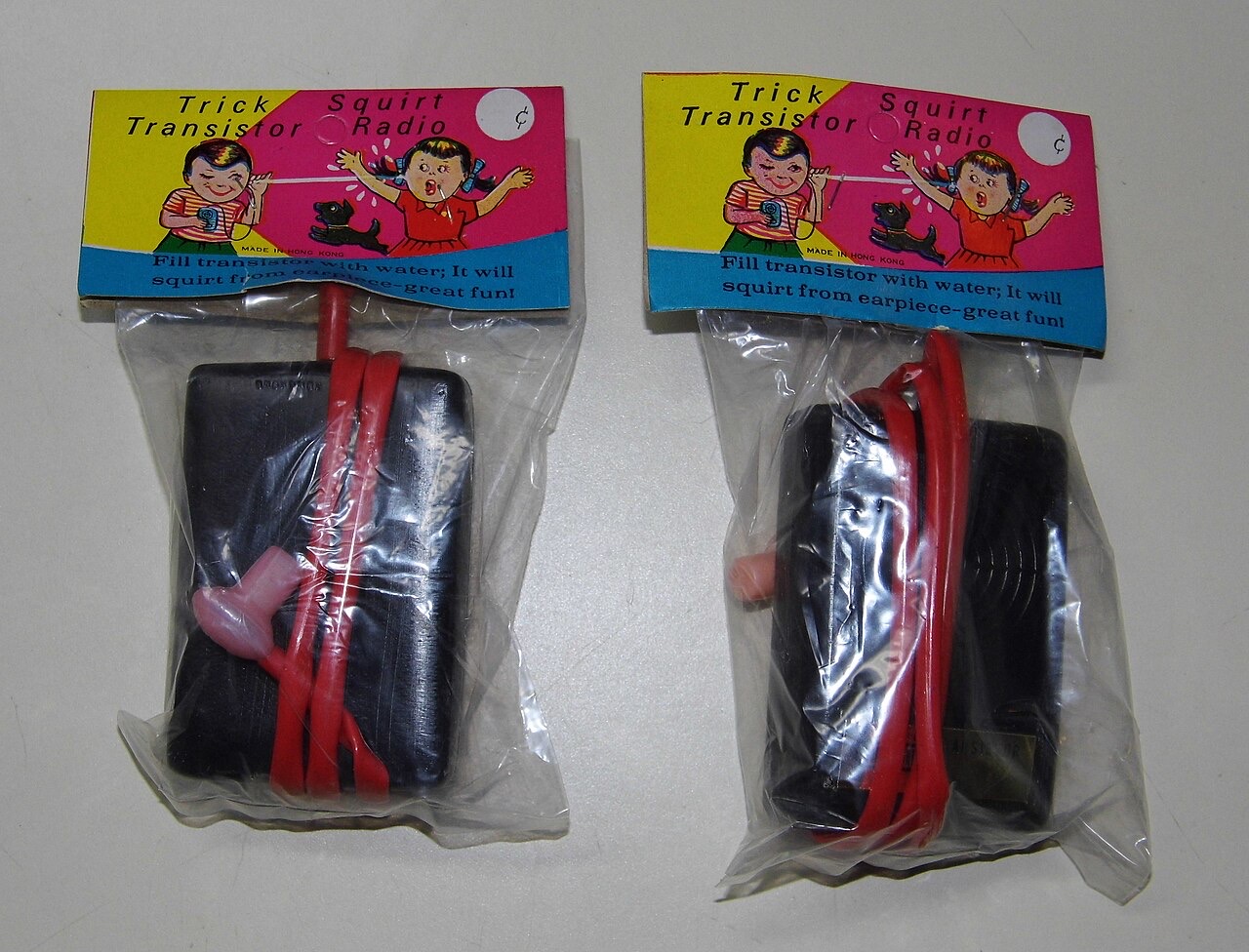 Two vintage dimestore novelty toys sealed in plastic bags with bright printed header cards: squirt guns molded to look like black transistor radios
