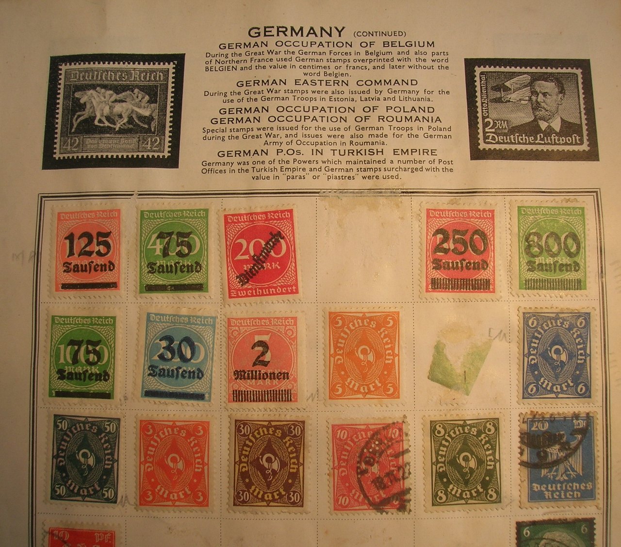 A page from an old stamp album with rows of small red, green, blue and brown postage stamps mounted under a printed heading