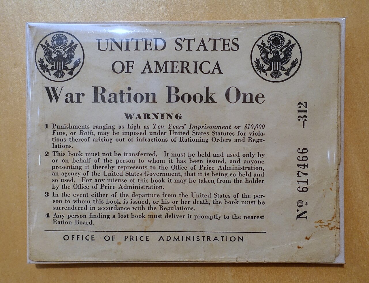 The worn tan cover of a United States War Ration Book One from the 1940s, printed with two eagles, a numbered serial, and four warning paragraphs