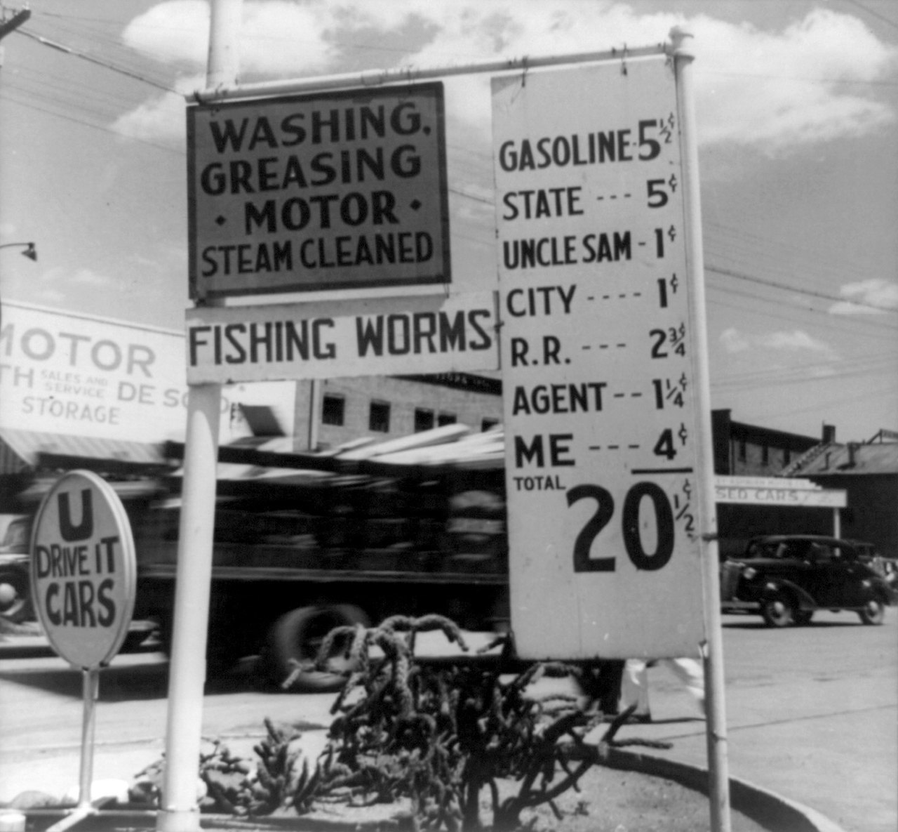 Black-and-white 1938 photograph of a hand-painted gas station sign that splits the price of a gallon into lines: gasoline, state, Uncle Sam, city, railroad, agent, and Me, with a total of twenty and a half cents