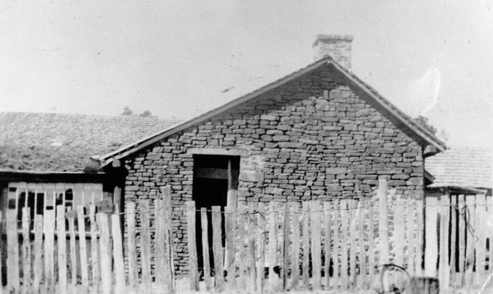An old stone cottage with a thatched roof and small windows, photographed in black and white