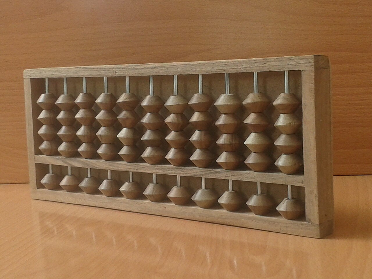 A wooden Japanese abacus standing on a desk: a long frame divided by a bar, with one bead above the bar on each rod and four beads below it