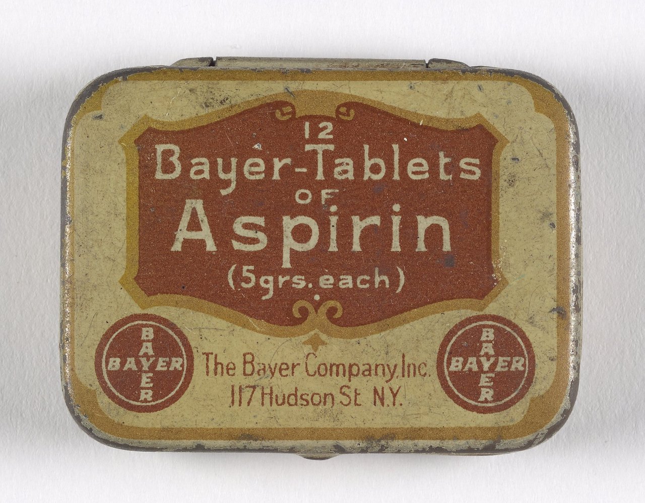 A small worn rectangular metal tin with a yellow and brown label reading 12 Bayer-Tablets of Aspirin, 5 grs. each, The Bayer Company Inc., 117 Hudson St. N.Y.