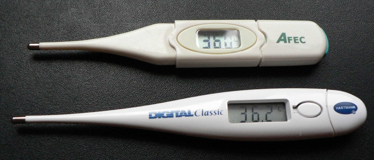 Two white digital fever thermometers lie side by side on a black surface, their small screens reading 36.0 and 36.2 degrees