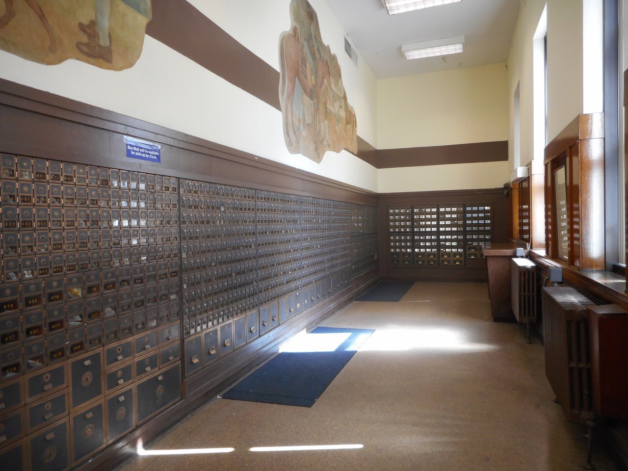 A long post office lobby lined floor to ceiling with hundreds of small numbered brass box doors, each with its own keyhole