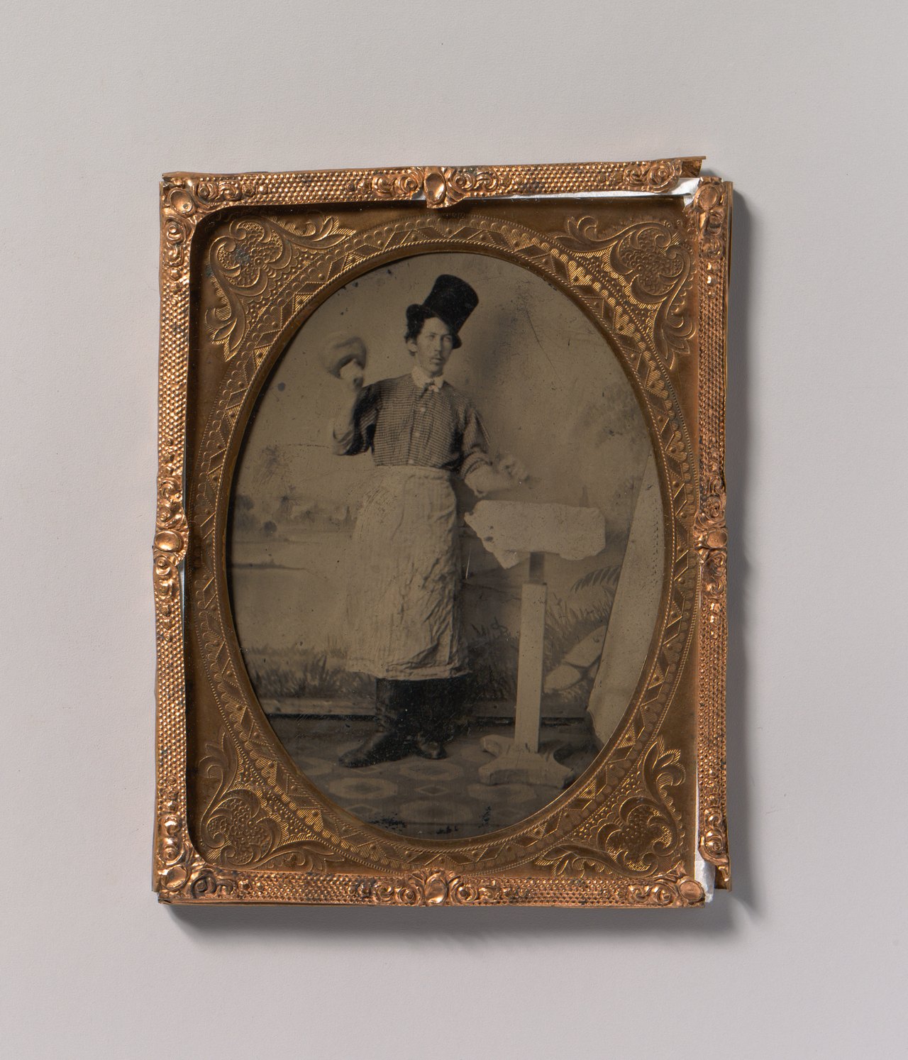 An early photographic portrait in an ornate gilt frame showing a stone mason in a top hat and work apron, a mallet raised in one hand and a chisel held to a block