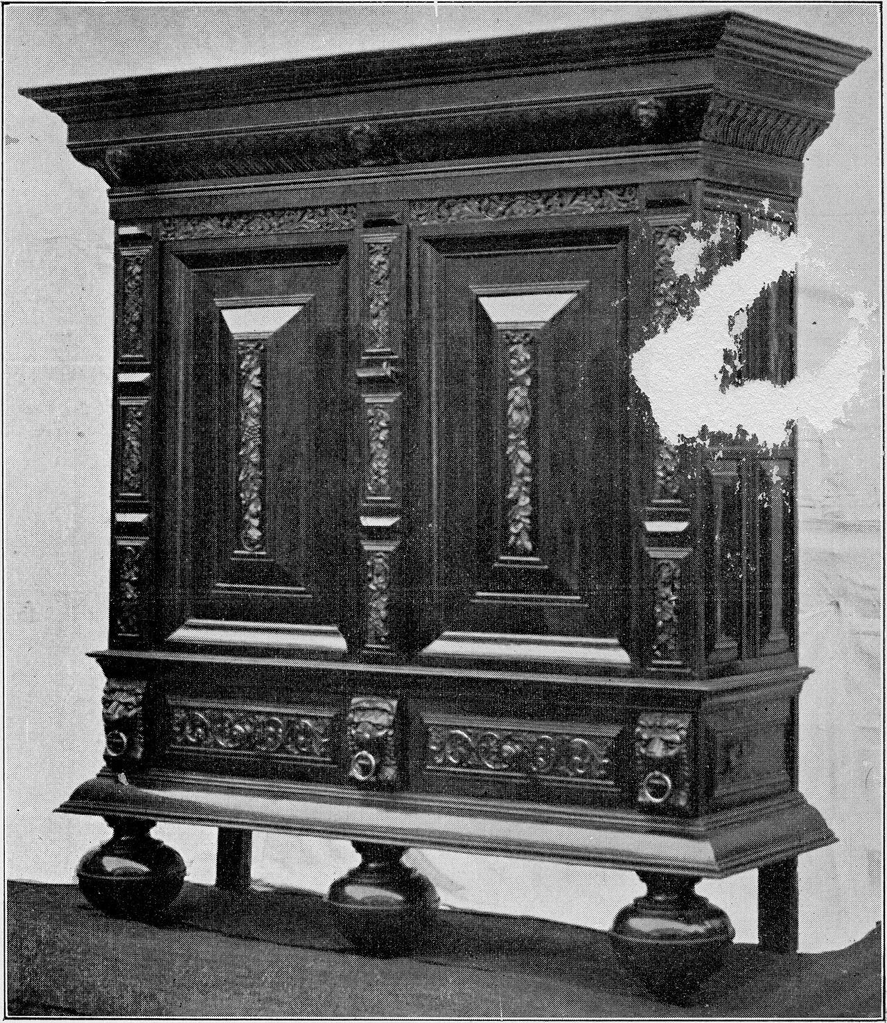 An old black-and-white photograph of a tall, heavily carved two-door wooden cupboard standing on three large ball feet, with a deep cornice across the top