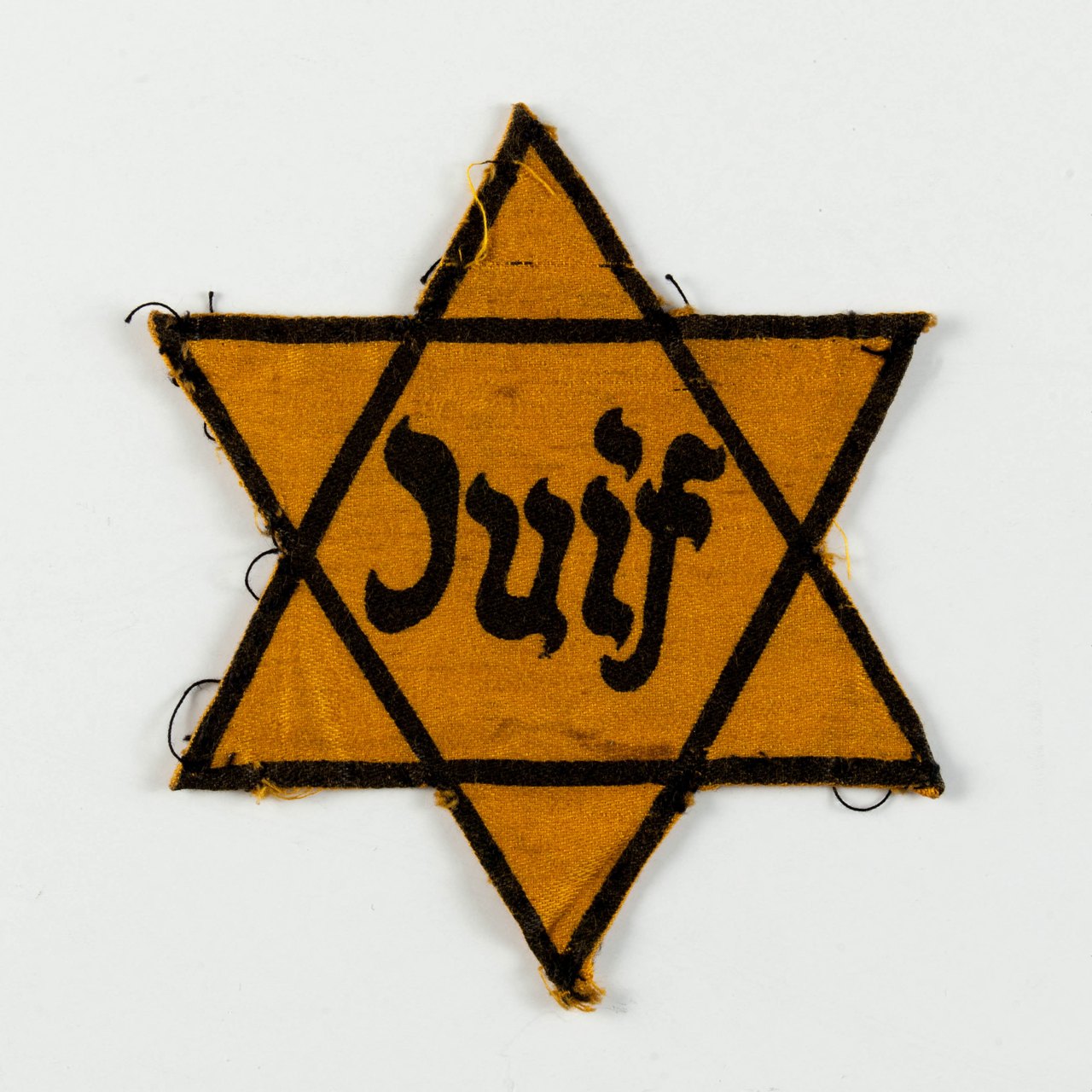 A worn yellow cloth six-pointed star outlined in black, with the word Juif printed across its center in black letters, photographed flat against a white background