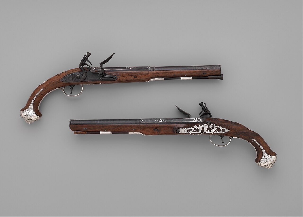 A matched pair of flintlock pistols with dark walnut stocks, long steel barrels and ornate silver mounts, arranged head to tail on a plain gray background