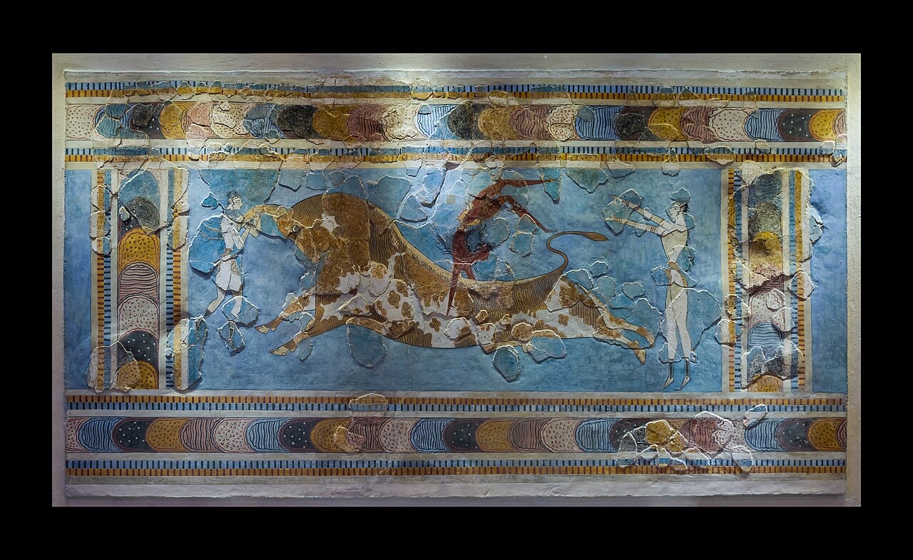 A restored Minoan wall painting: a huge charging bull at full stretch, with one athlete grasping its horns, one vaulting over its back, and one standing behind with arms raised