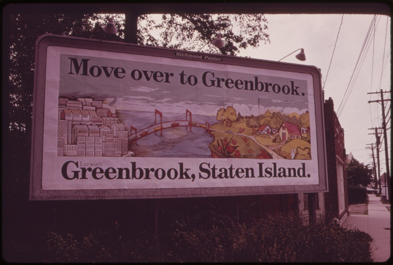 A large roadside billboard on a New York street in 1973 reads Move over to Greenbrook, Greenbrook, Staten Island, above a painted scene of a bridge and tidy houses