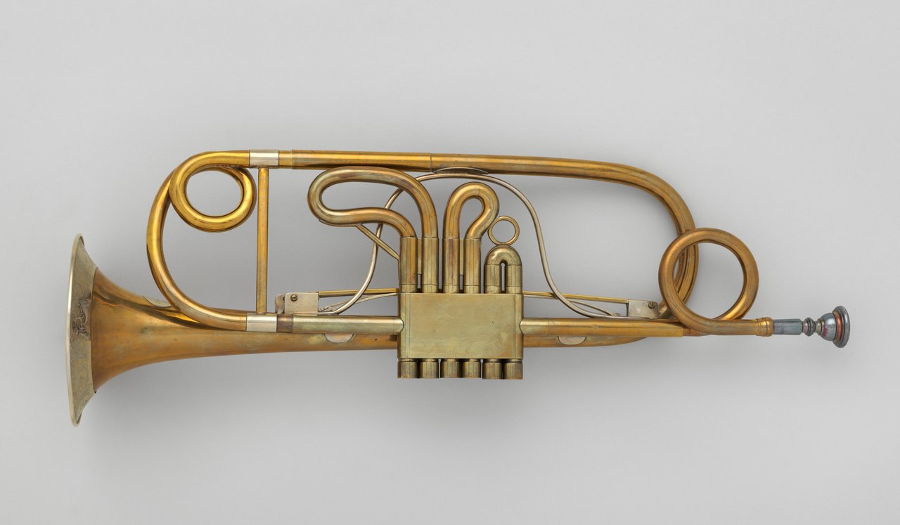 A brass valve trumpet photographed side on against a plain background, its coiled tubing, three finger valves and flared bell all clearly visible