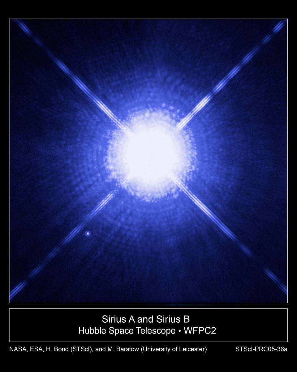 A brilliant blue-white star flaring with four long diffraction spikes against black space, with a tiny point of light at its lower left