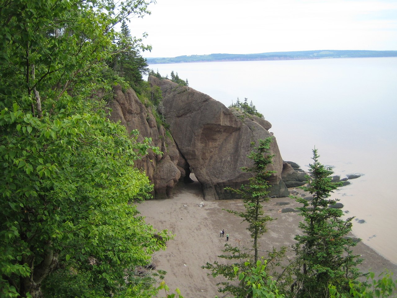 A wide bay at low tide, the water pulled far back to leave bare brown sea floor and standing rock stacks where boats would otherwise float