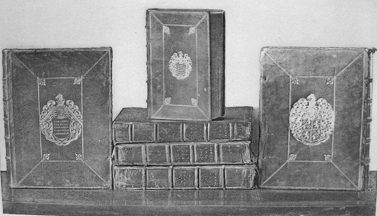 Three leather-bound manuscript volumes standing upright on a stack of further volumes, each cover stamped with an ornate crest