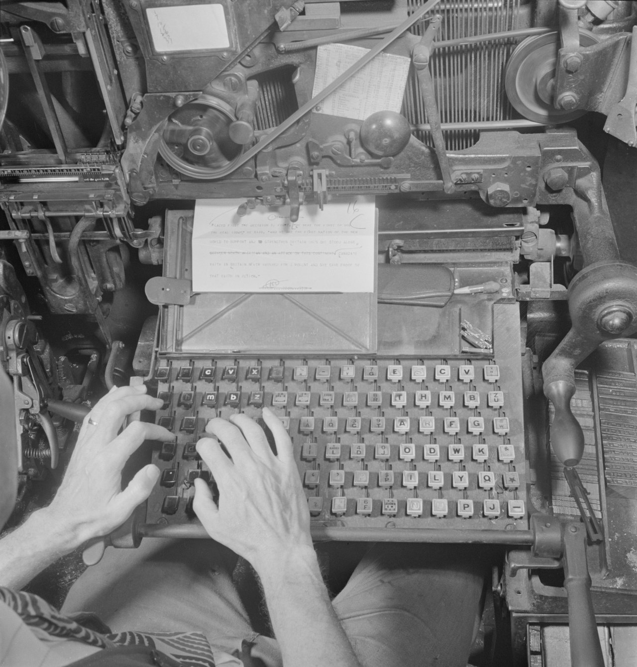 A close view of two hands working the keyboard of a linotype machine in a 1942 newspaper composing room, surrounded by levers and metal type mechanisms