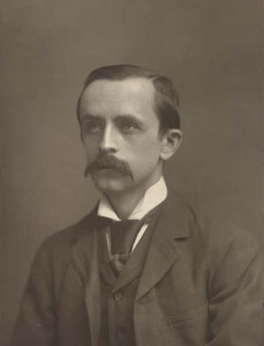 A sepia studio portrait of a man in a dark jacket and high collar, with a full moustache, looking slightly away from the camera