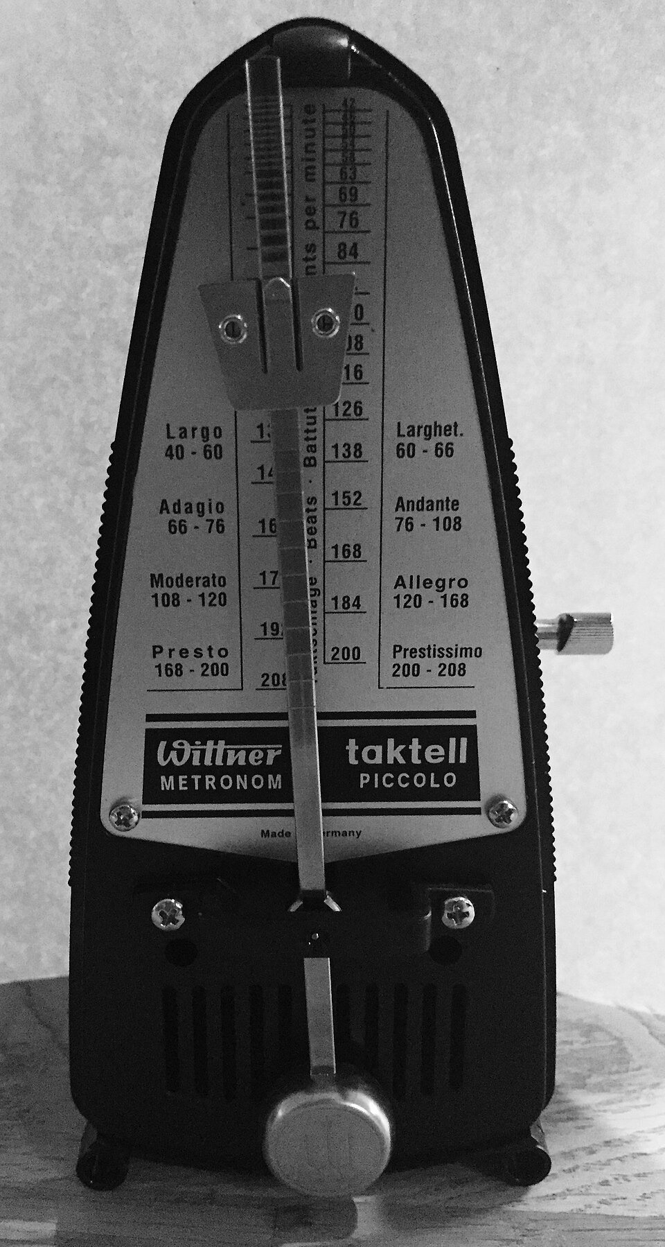 A black pyramid-shaped mechanical metronome with a swinging arm, a sliding weight and a printed tempo scale